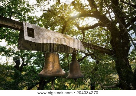Georgian orthodox prayer bells hang on tree with sunlight in Katskhi village