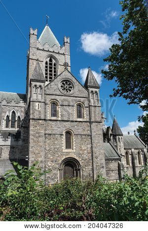 Dublin Ireland - August 7 2017: Gray stone bell tower and chancel of Christ Church Cathedral against blue sky with white clouds. Green vegetation.