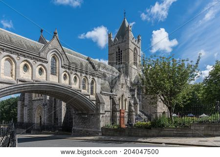 Dublin Ireland - August 7 2017: Gray stone Christ Church Cathedral with overpass link to Dublinia building against blue sky with white clouds. Green vegetation. Art market in back.