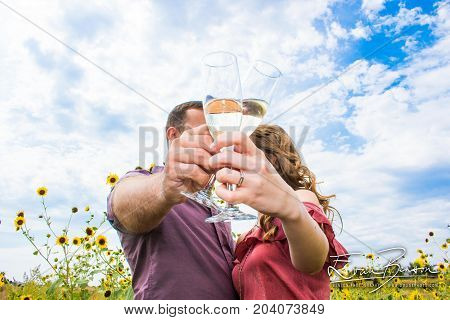 Happy Couple Engagement Photo Just Engaged Toasting With Champagne With Blue Sky and Wild Flowers in the Country Just Married