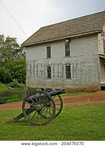 a civil war cannon in front of an old gristmill