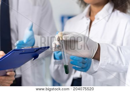 Group Of Laboratory Scientists Examining Test Tube Making Notes Discuss Experiment Or Reseach Results Wearing Protective Coats Gloves, Workers In Lab