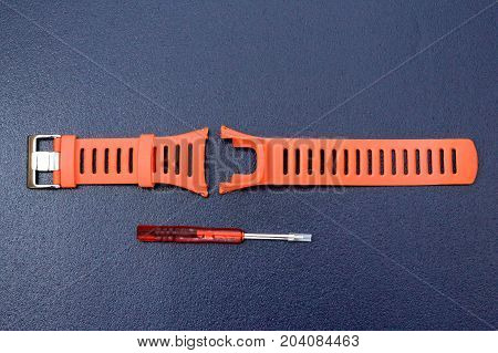 Orange watchband rubber skin & repairing tool kit for adjusting watchband on isolated blue background.