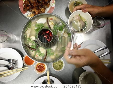 Woman Hands Holding A Mug Of Tom Yam Mixed Sea Food With Mushroom In Hot Pot With Family Dinner On T