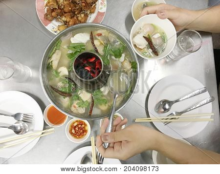 Woman Hands Holding A Mug Of Tom Yam Mixed Sea Food With Mushroom In Hot Pot With Family Dinner On T