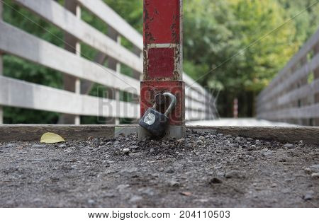 With a lock pad locked across the bridge. Padlock detail. In the background are trees.
