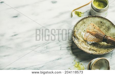 Flat-lay of Japanese tools for brewing matcha green tea. Matcha powder in tin can, Chashaku spoon, Chasen bamboo whisk, Chawan bowl over grey marble background, selective focus, copy space