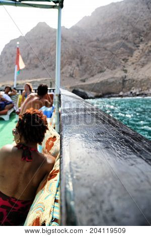 Tourist in swimwear relaxing on a boat enjoying view on a sea and Al Hajar Mountains in Oman sunny hot day summer vacation