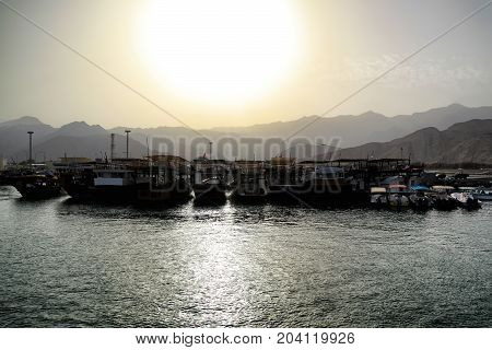 View on a boats docked at the little harbour in Oman beautiful sunset over Al Hajar Mountains