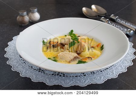 Creamy soup with fish fillet and mussels in a white plate on a white cloth on a grey abstract background. Healthy eating concept. Mediterranean lifestyle