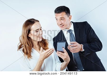 Did you know. Waist up shot of friendly business people gesturing while taking a break and gossiping over something while using a smartphone.