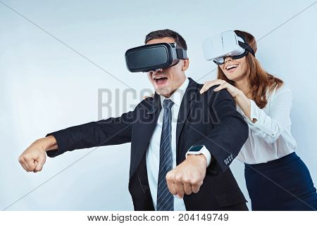 I believe in you. Successful man pretending to drive a motor bike with his colleague behind while both wearing a VR headset and having fun.