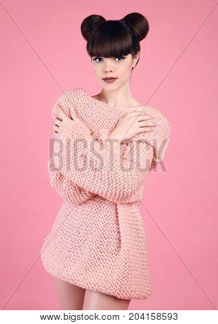 Fashion studio teen look style over pink. Fashionable young girl wears wool knitting sweater. Brunette with matte lips and bun hairstyle in soft pullover posing isolated on studio background.