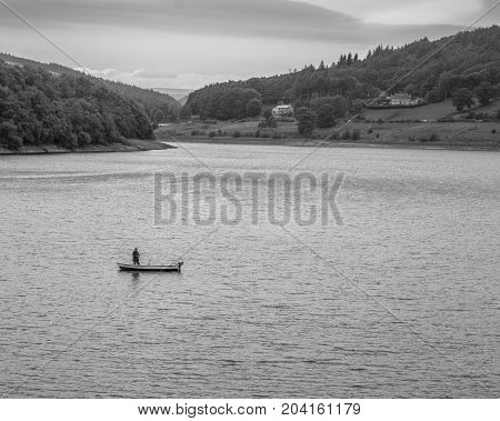 Lone fly fisherman on Ladybower Reservoir. Fly fisherman in a small lake boat fisherman standing in the boat casting out line.