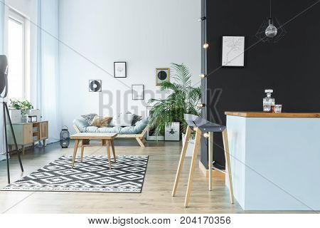 Wooden table in spacious monochromatic living room with settee and barstool at kitchen island