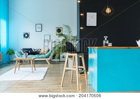 Black barstool at blue kitchen island with decanter in living room with table on white carpet
