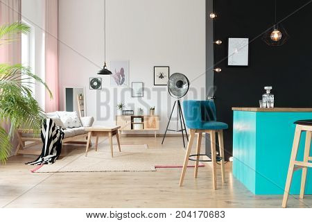 Designer lamp in open relax space with suede barstool at blue minibar against black wall