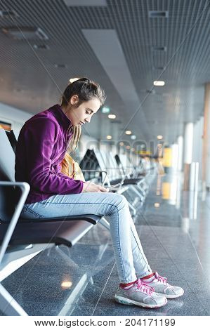 Girl at the airport window sits on the banch and looking at smartphone