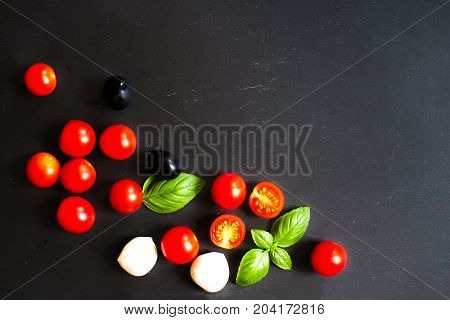 Food ingredients - Tomatoes basil leaf mozarella cheese and black olives. Fresh vegetables and fresh herbs over dark chalk board background. Healthy food diet nutrition concept.
