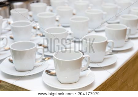 Many rows of white coffee cup with saucer and teaspoon on table and coffee maker background