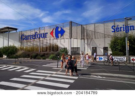 Serignan, France - August 20 2017: Shoppers Outside The Carrefour Supermarket In Serignan On A Sunny
