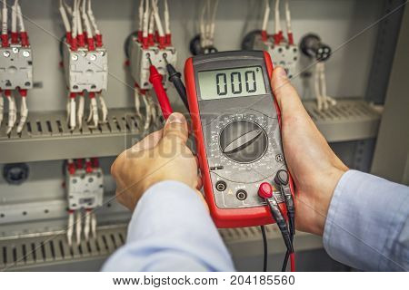 Engineer's hands with multimeter close-up against background of terminal rows of electric automation panel. engineer tests industrial electrical circuits with multimeter in control terminal box.