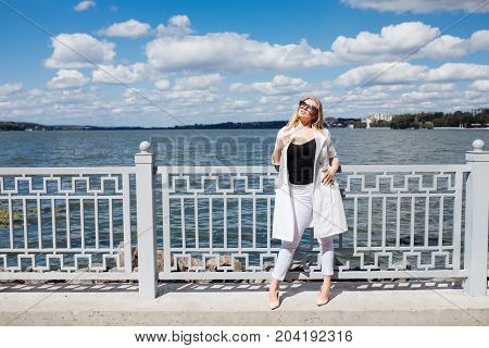 Pretty Young Blonde Woman Standing At The Embankment Seashore In The Rays Of The Setting Sun