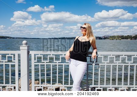 Pretty Young Blonde Woman Standing At The Embankment Seashore In The Rays Of The Setting Sun
