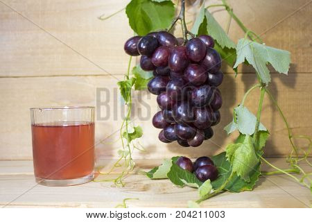 grapes on a brown background. a bunch of grapes. grapes, green leaves. dark blue grapes. juice in a glass