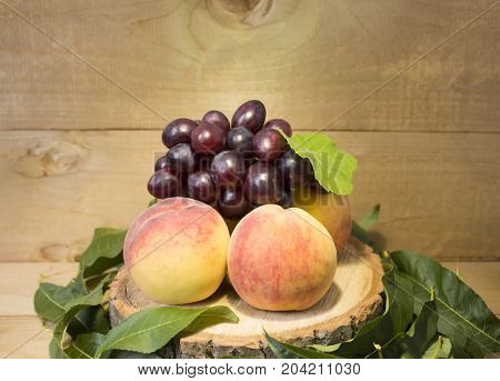 peaches and grape brown background. grapes with green leaves. a bunch of grapes. in green leaves. peaches with dark blue grapes.