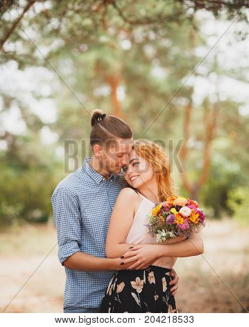 Image of love story in the forest. Beautifull couple kissing and embracing near the shore of a mountain river with decorated table. Girl smiling in the arms.
