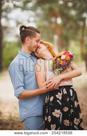 Image of love story in the forest. Beautifull couple kissing and embracing near the shore of a mountain river with decorated table. Girl smiling in the arms.