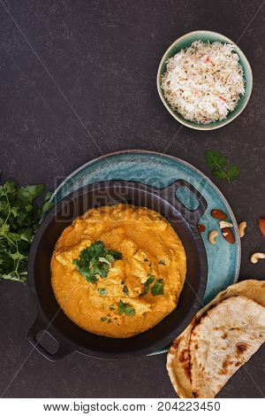 Chicken Korma, traditional Indian dish with nuts, jeera rice and naan bread on rustic surface. Top view, blank space