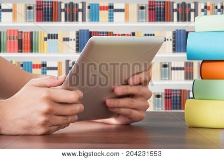 Close-up Of Hand Holding Digital Tablet On Table In The Library