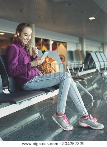 Girl at the airport window sits on the banch and looking at smartphone