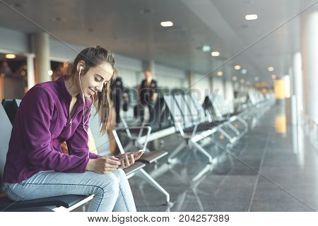 Girl at the airport window sits on the banch and looking at smartphone