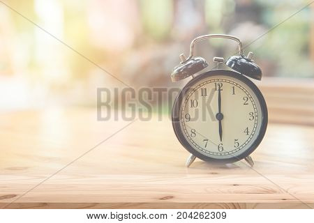 Retro clock at 6 o'clock on wood table foreground with blur light nature background