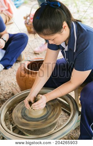 Student learning to hand making a clay or mud pot on a potters wheel in original process.