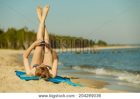 Summertime pleasures enjoying vacation concept. Woman in bikini sunbathing and relaxing on beach using smartphone checking social media and writing sms