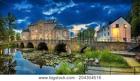 Panoramic HDR image of Orebro Castle and bridge reflecting in water of Svartan river at dusk Sweden