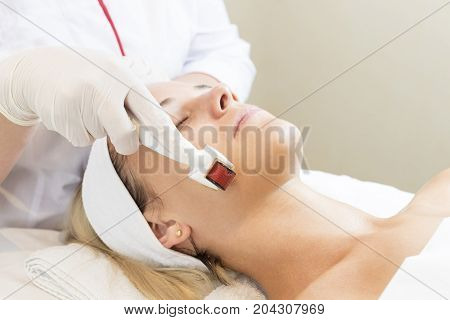 The woman undergoes the procedure of medical micro needle therapy with a modern medical instrument derma roller.
