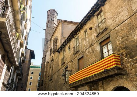 Catalan Flag, Hanging On A Balcony, In The Gothic Quarter Of Barcelona. Belfry Of The Pine Church In