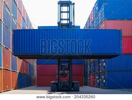 Forklift truck lifting cargo container in shipping yard or dock yard against sunrise sky with cargo container stack in background for transportation import, Export and logistic industrial concept