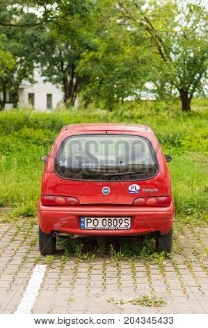 Red Fiat Seicento parked on a parking spot with green weeds on August 2017 in Poznan Poland
