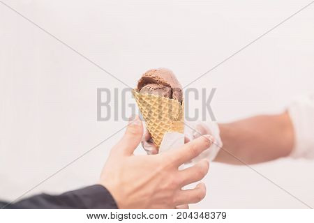 Close-up hands of buyer and seller with ice-cream chocolate, coffee, cream-brule in waffle cone. Delicious cooling portion on hot day and just for fun. Real scene in store on light background. Uninsulated. Copy space, for background