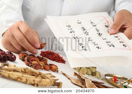 Asiatische Kräuterkundler machen ein Rezept, chinesische Schriftzeichen sind Namen für die Kräuter.
