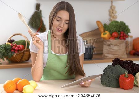 Young  woman is making online shopping by tablet computer and credit card. Housewife found new recipe for  cooking in a kitchen.