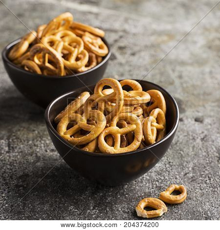 Salted pretzels in two ceramic matte dark bowls on a gray stone grunge background. Selective focus