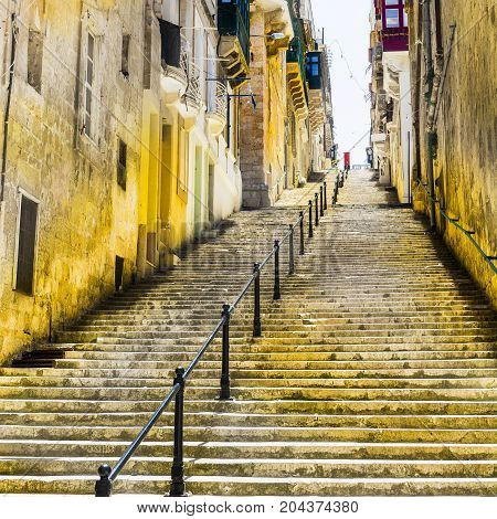 Typical narrow street with stairs on the island of Malta. Buildings with traditional colorful maltese balconies in historical part of Valletta.