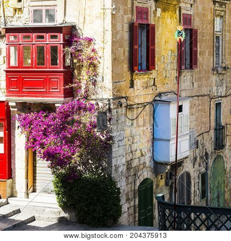 Building with traditional colorful maltese balcony in historical part of Valletta. Red windows decoreted with begonville on the facade of a house in Malta